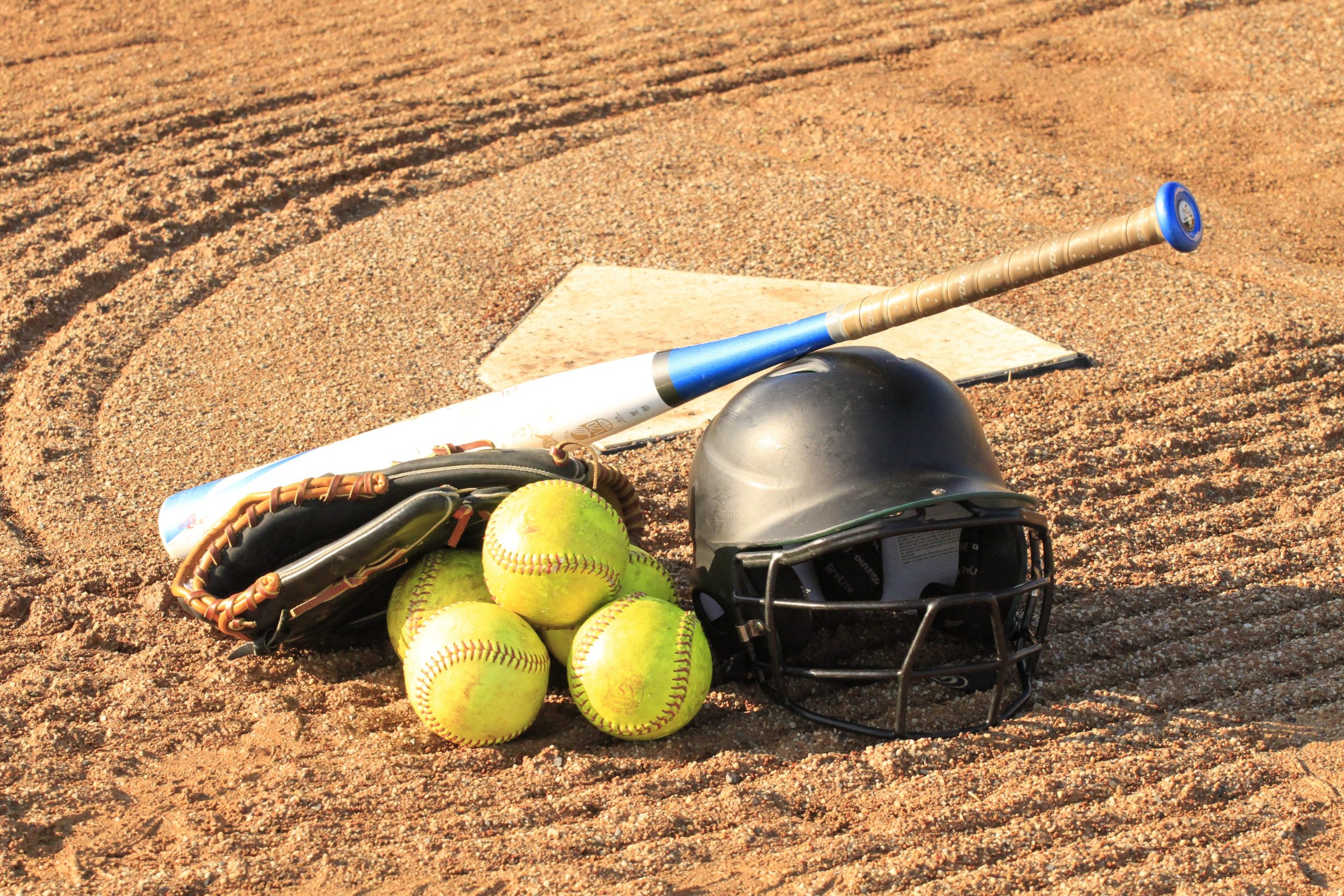 softball equipment helmet, balls, and bat, next to a pitching spot.