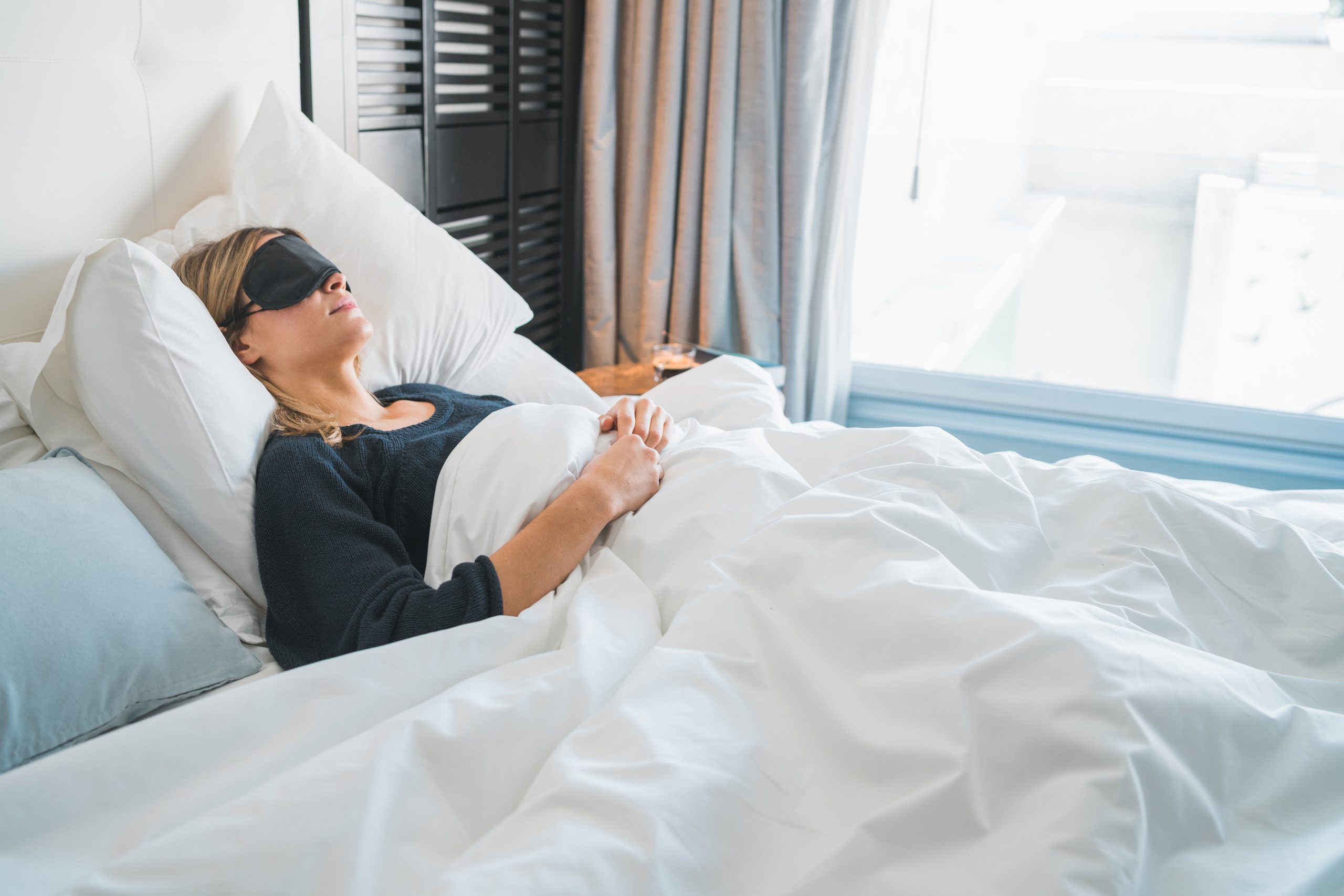woman sleeping in a big bed wearing a face mask during daylight hours